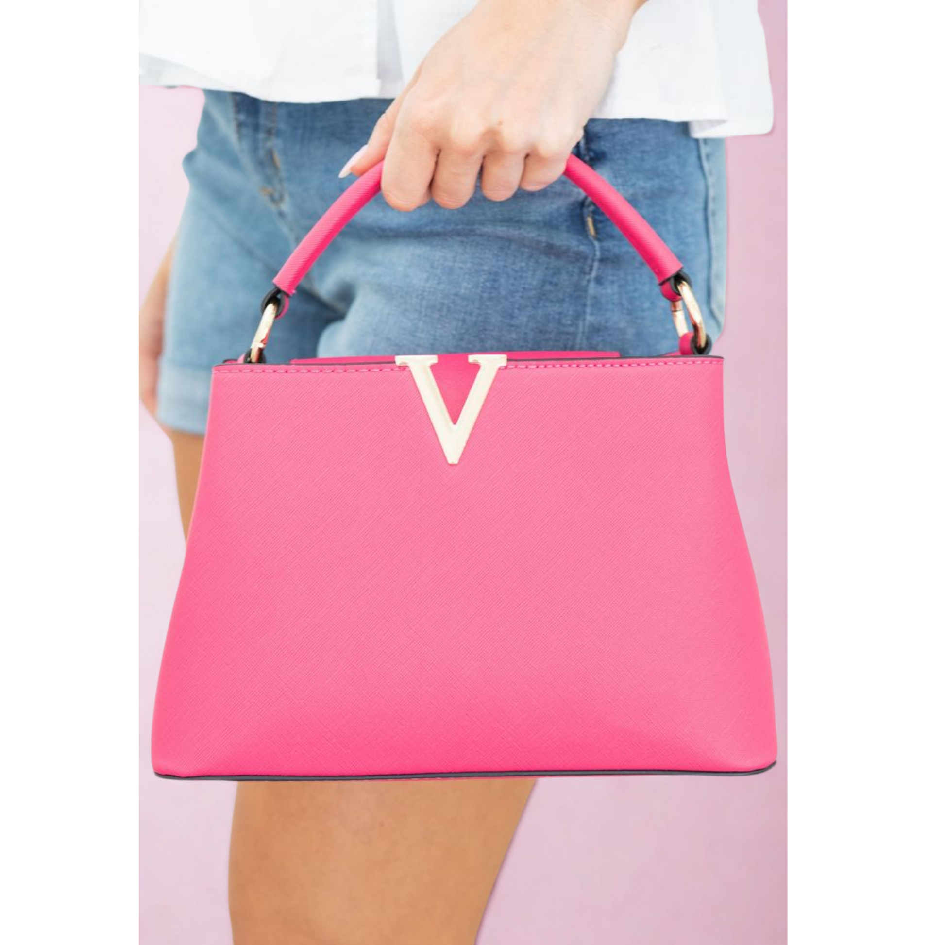 Pink handbag with a white logo held by a person wearing blue jeans on a pink background