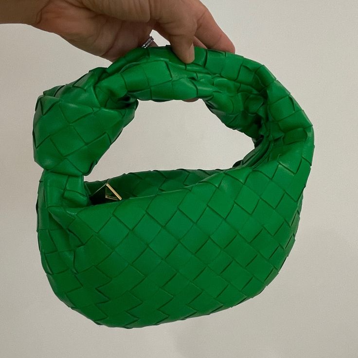 Green woven handbag held by a hand against a plain background