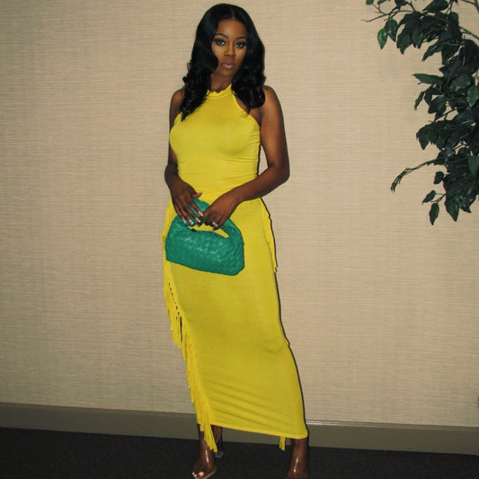Woman in a yellow dress holding a green clutch against a beige wall with a plant.