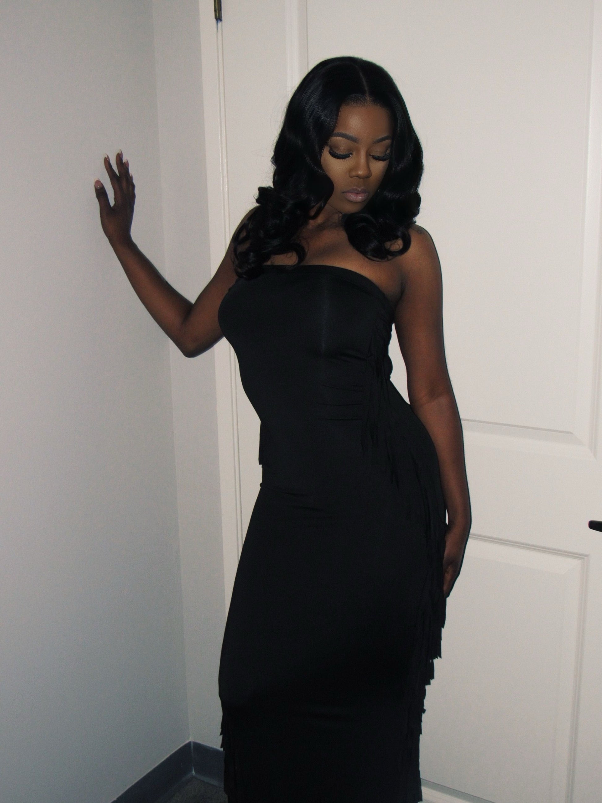 Woman wearing a black strapless dress against a white wall.